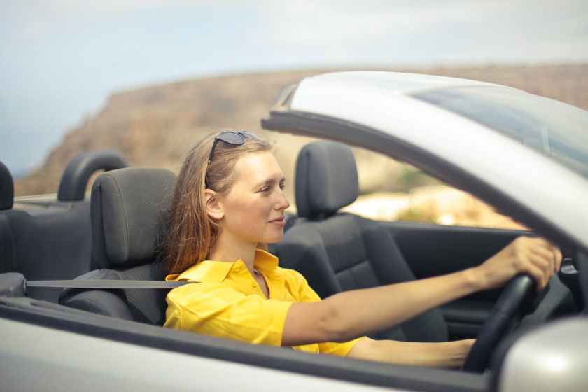 A woman in a yellow shirt driving a car.